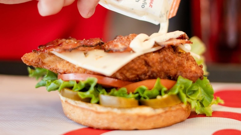A close-up of a person squeezing sauce onto a Chick-fil-A Jalapeño Ranch Club sandwich