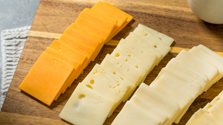 Sliced cheeses on a wooden cutting board