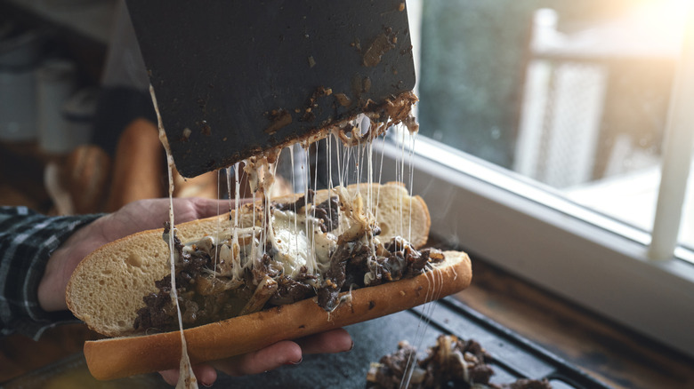 Cheesesteak meat being put onto a roll with melted cheese