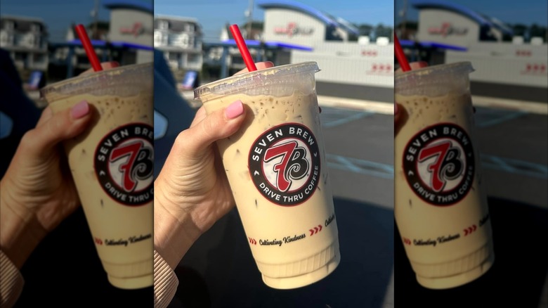 Hand holding Blondie iced coffee beverage from 7 Brew coffee in plastic cup with red straw