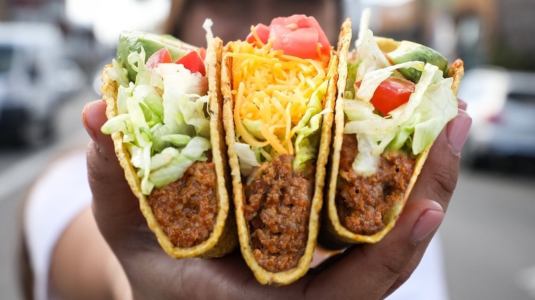 Person holding three crunchy beef tacos from Del Taco