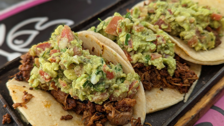 three pork tacos with guacamole on top