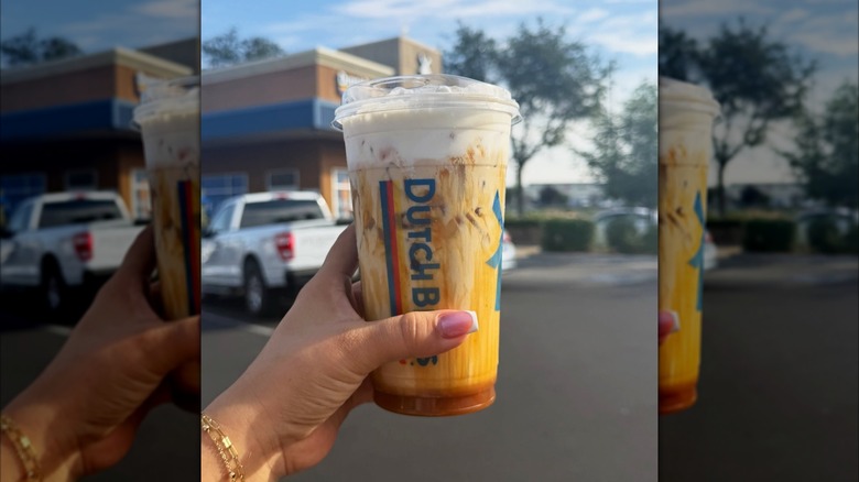 Hand holding a plastic cup of iced pumpkin spice latte with Soft Top topping from Dutch Bros
