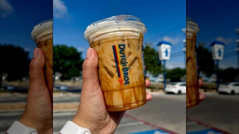 Hand holding iced latte drink with syrup from Dutch Bros in outdoor setting