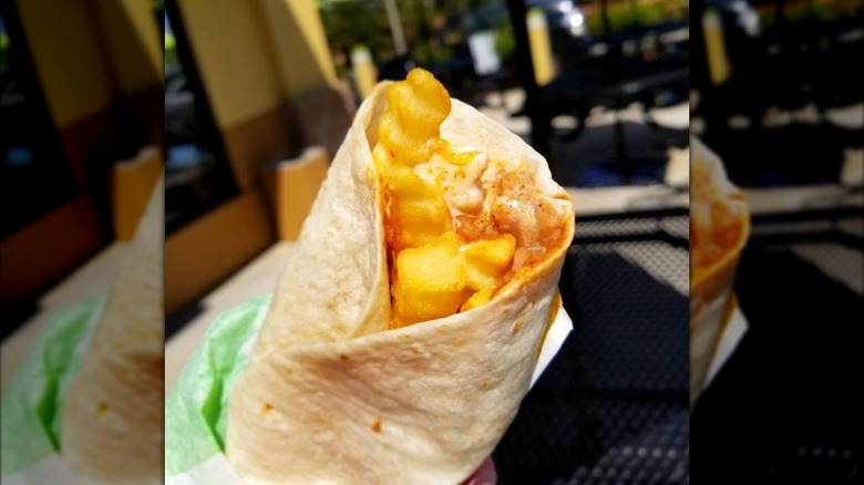 Someone holding a Del Taco Bold burrio showing beans, source cream, and crinkle cut fries inside a tortilla