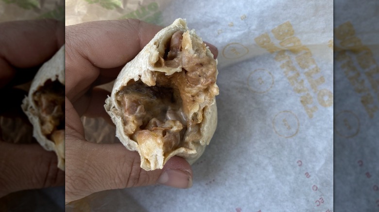 Someone holding a half-eaten stoner-style burrito from Del Taco, showing off the filling