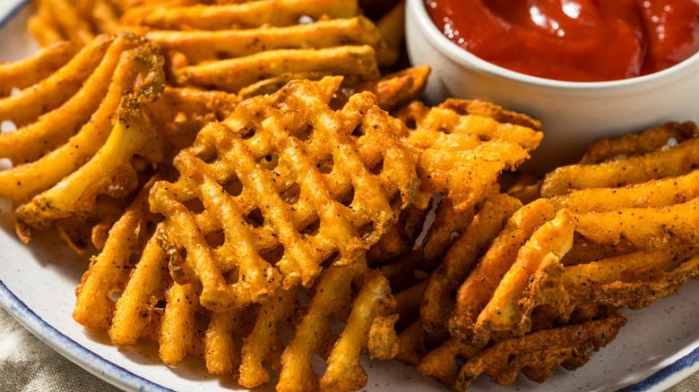 A plate of extra crispy waffle fries with a cup of ketchup.