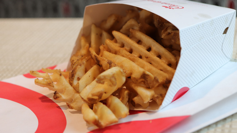 Chick-fil-A waffle fries spill out of a box and onto a paper bag.