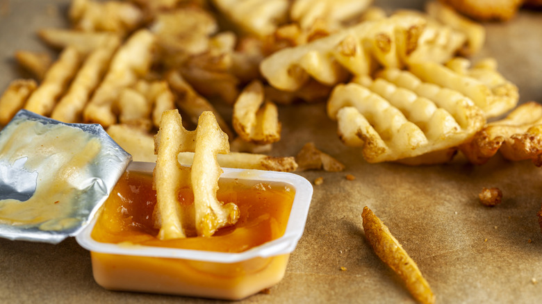 A waffle fry being dipped in a packet of sauce.