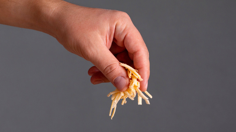 A hand pinching shredded cheese