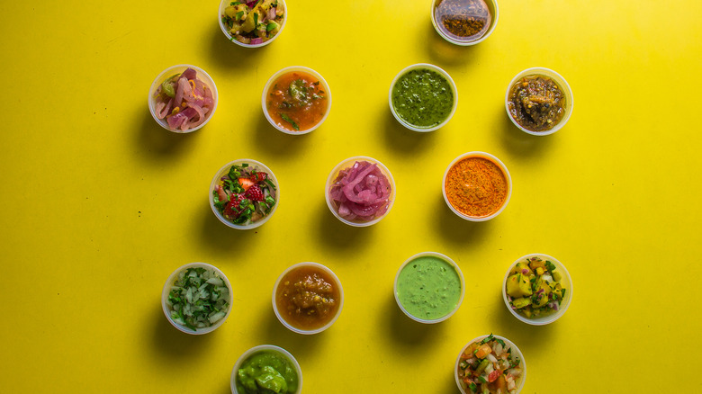 Cups containing various salsas sitting on a yellow surface
