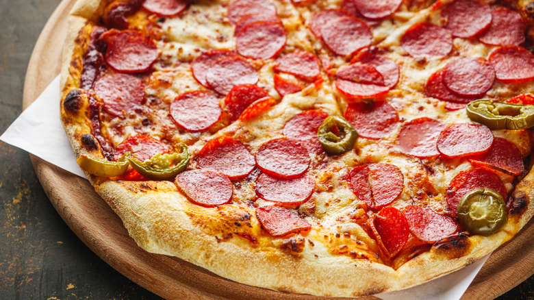 A pepperoni and jalapeno pizza sitting on a wooden pizza board