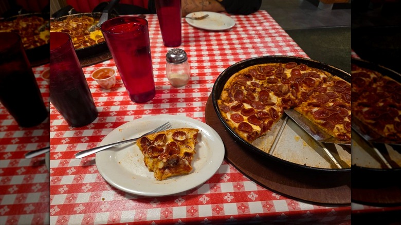 A Pizza Hut pizza in the pan top with Crispy cupped pepperoni, sitting on a table with cups and another Pizza