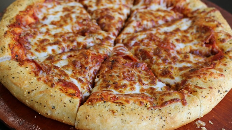 A full, sliced pizza with pepperoni under the cheese viewed from the side
