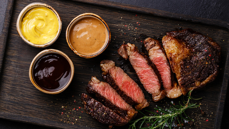 Three cups of dipping sauces sit next to a sliced ribeye steak.