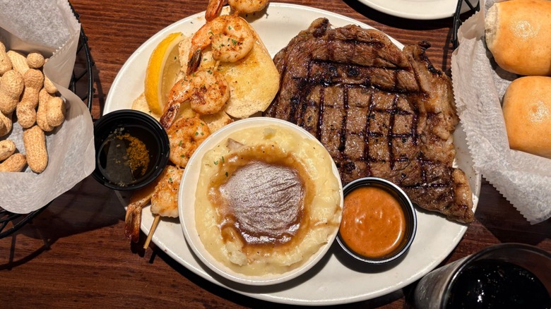 A Texas Roadhouse spread of ribeye steak with shrimp, mashed potatoes, unshelled peanuts, and dinner rolls