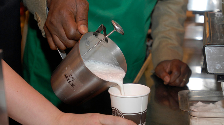 A close-up of a Starbucks barista adding steamed milk to an espresso drink