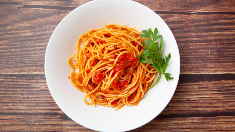 Spaghetti arrabbiata served on a white plate on a wooden table