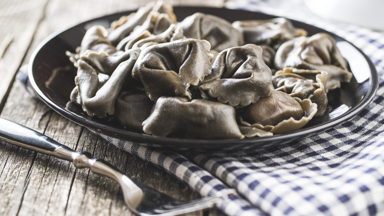 Squid ink tortellini placed on a checkered table napkin with a fork
