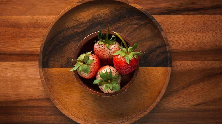 Dark acacia wood plate and a smaller bowl holding ripe strawberries