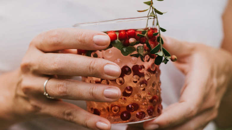 A person holds a glass of pink liquid with berries floating in it
