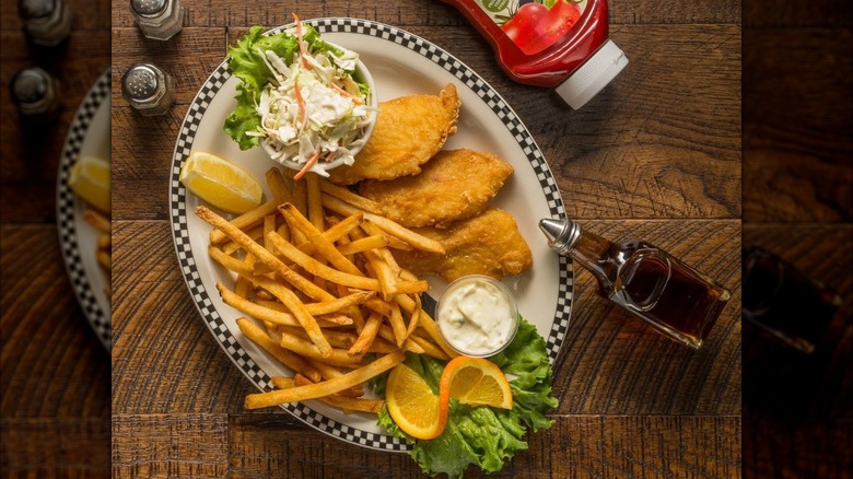 Fried fish, coleslaw, and fries from Black Bear Diner on black and white checkered rim plate on wooden table