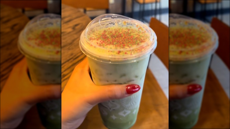 A woman holding a green iced matcha latte with red and green sprinkles