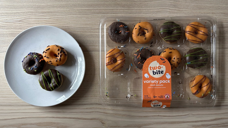 Package of Two-Bite Iced Donuts on wooden table with three pieces on plate