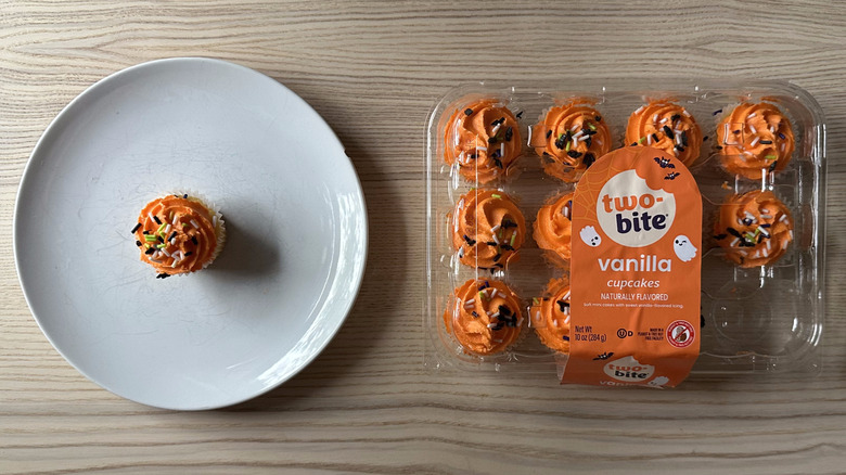 Package of Two-Bite Vanilla Cupcakes on wooden table with one on plate