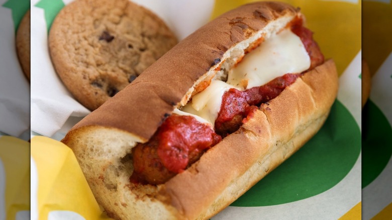 A 6-inch Subway meatball sub with marinara sauce and cheese next to a cookie