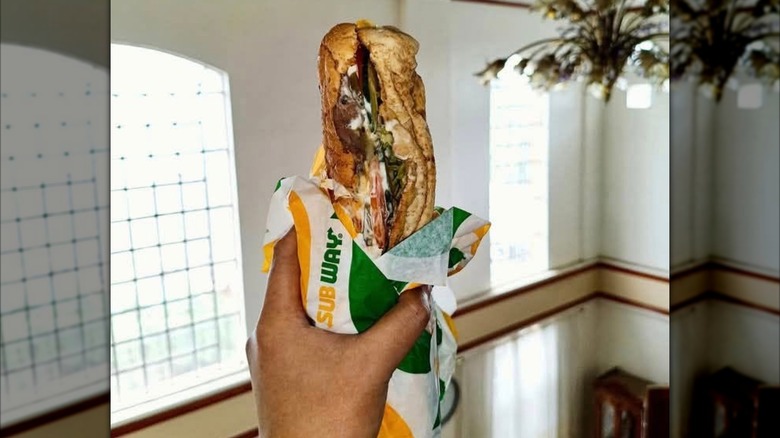A 6-inch Subway roast beef sandwich with meat and lettuce hanging out the sides sitting on Subway paper