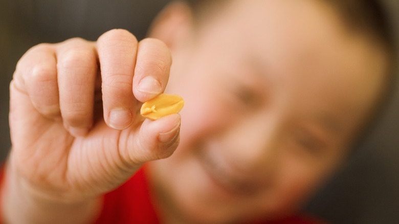 a child's hand holding half of a peanut up to the camera, with their smiling face blurry in the background
