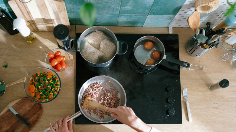 Overhead view of a woman cooking a variety of different types of food at once on an induction range