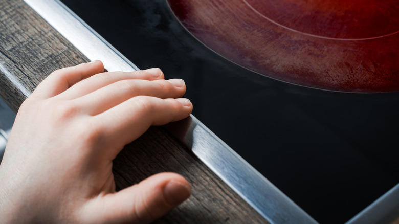A child's hand touching an induction cooktop with an active burner
