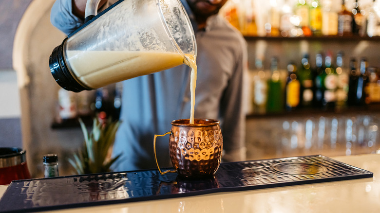 Bartender pouring a frozen cocktail from a blender into a copper mug