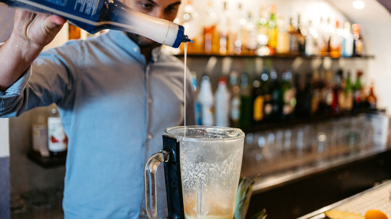 A bartender pouring sweet coconut syrup into a blender