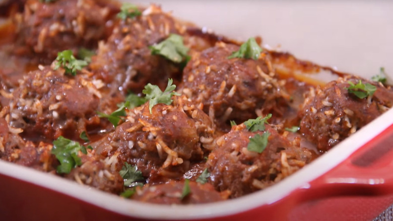 porcupine meatballs in a baking dish with tomato sauce and herb garnish