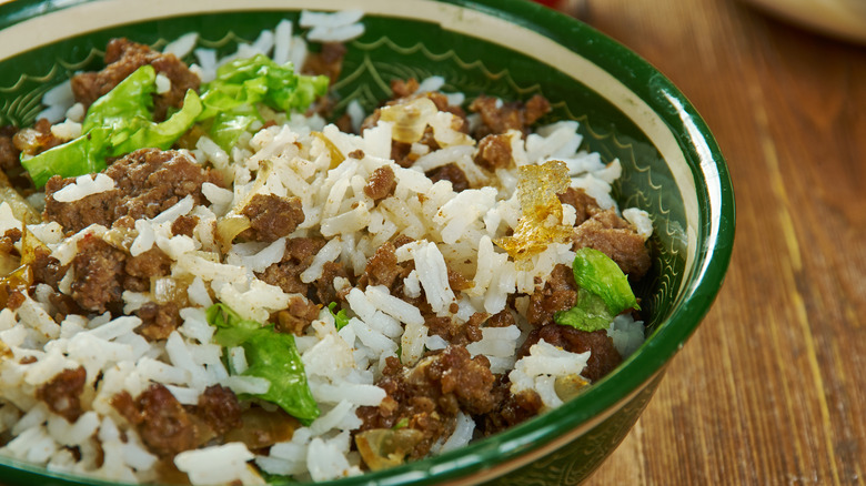 A casserole made of ground beef rice onions and peppers in a green and white bowl on a wooden table