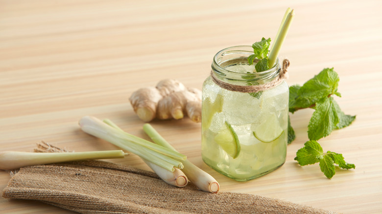 Cocktail in Mason jar next to lemongrass, ginger, and mint