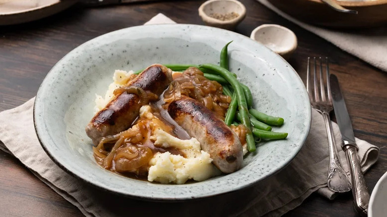 a bowl with bangers and mash covered in gravy and a side of green beans