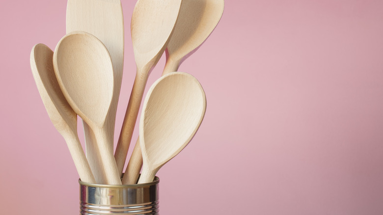 Tin can holding wooden spoons against a light pink backdrop.