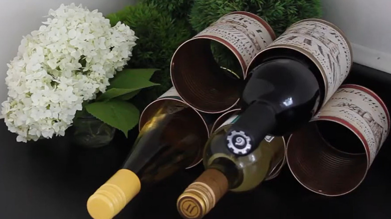 Wine rack made from tin cans with white hydrangeas on the table next to it.
