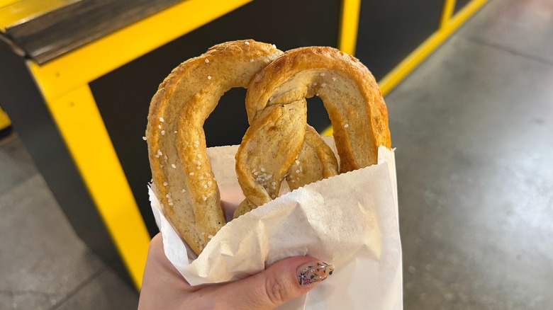 Hand holding soft pretzel in white paper