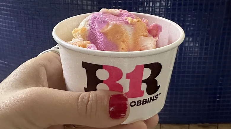 A person holding a cup of Baskin Robins' Rainbow Sherbet colorful scoop