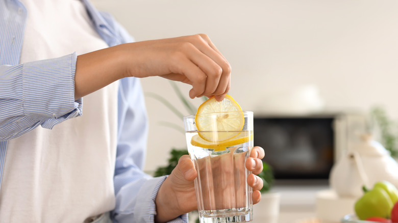 woman putting lemon slice into glass of water in kitchen
