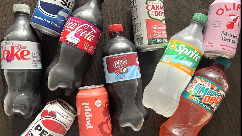 10 bottles and cans of new 2026 soda flavors laid on table.