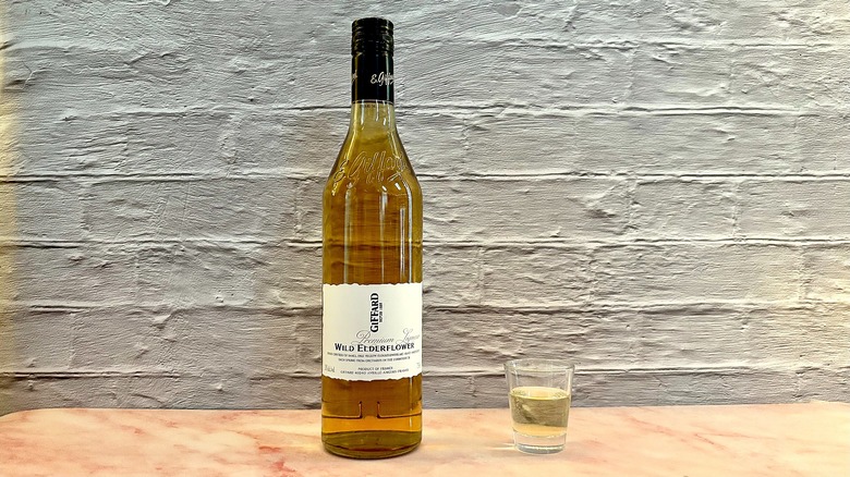 Shot glass of Giffard Elderflower liqueur on table next to bottle