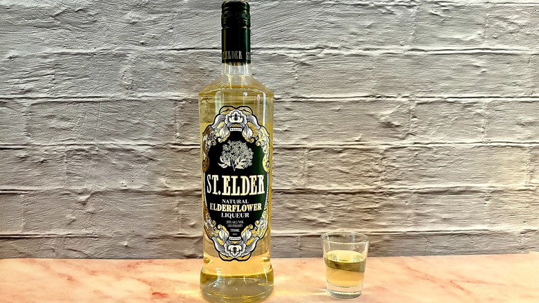 Shot glass of St. Elder Elderflower liqueur on table next to bottle