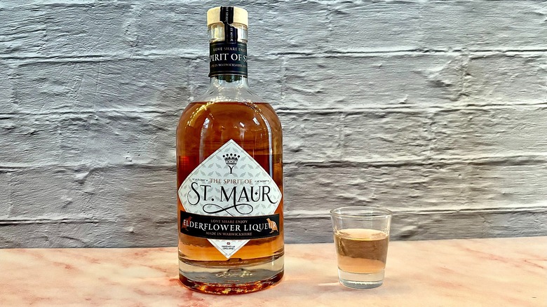 Shot glass of St. Maur Elderflower liqueur on table next to bottle