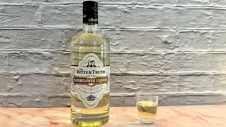 Shot glass of The Bitter Truth Elderflower liqueur on table next to bottle